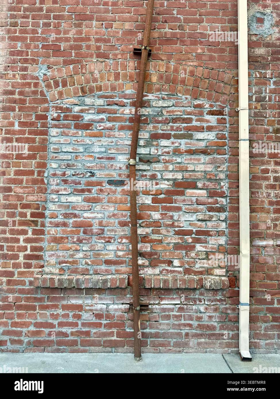 Verwitterte Ziegelwand mit versiegeltem Bogen und Rostrohr - Smartphone-aufgenommenes Stockfoto