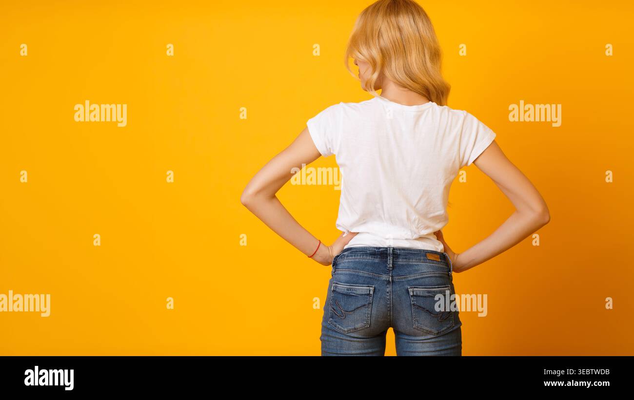 Die stylische Frau mit weißem Hemd und blauer Jeans posiert vor einem leuchtenden gelben Hintergrund Stockfoto