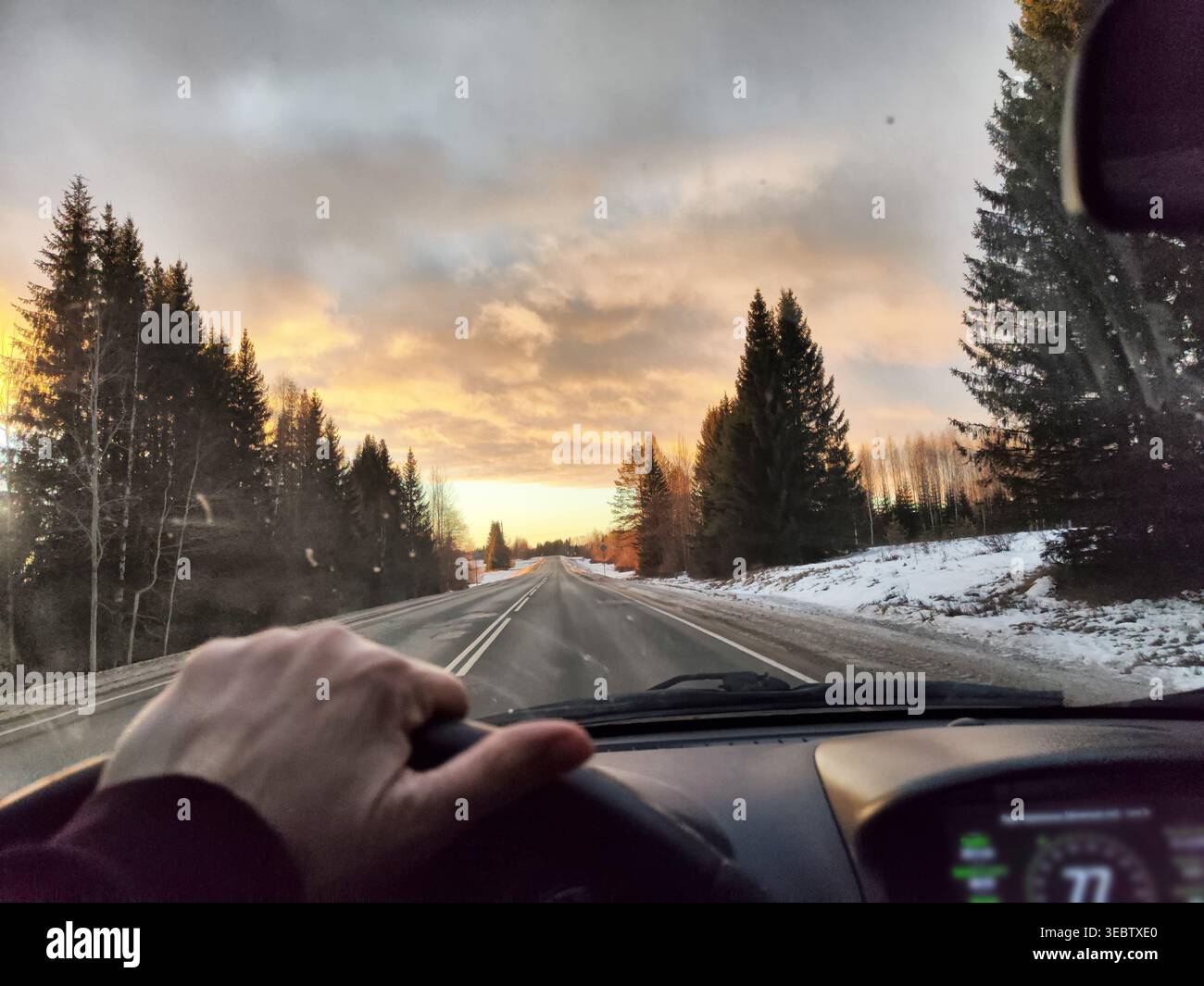 Ein Fahrer genießt einen Winterausflug bei Sonnenuntergang und blickt aus dem Autofenster auf die Straße und die Bäume entlang der Autobahn. Stockfoto