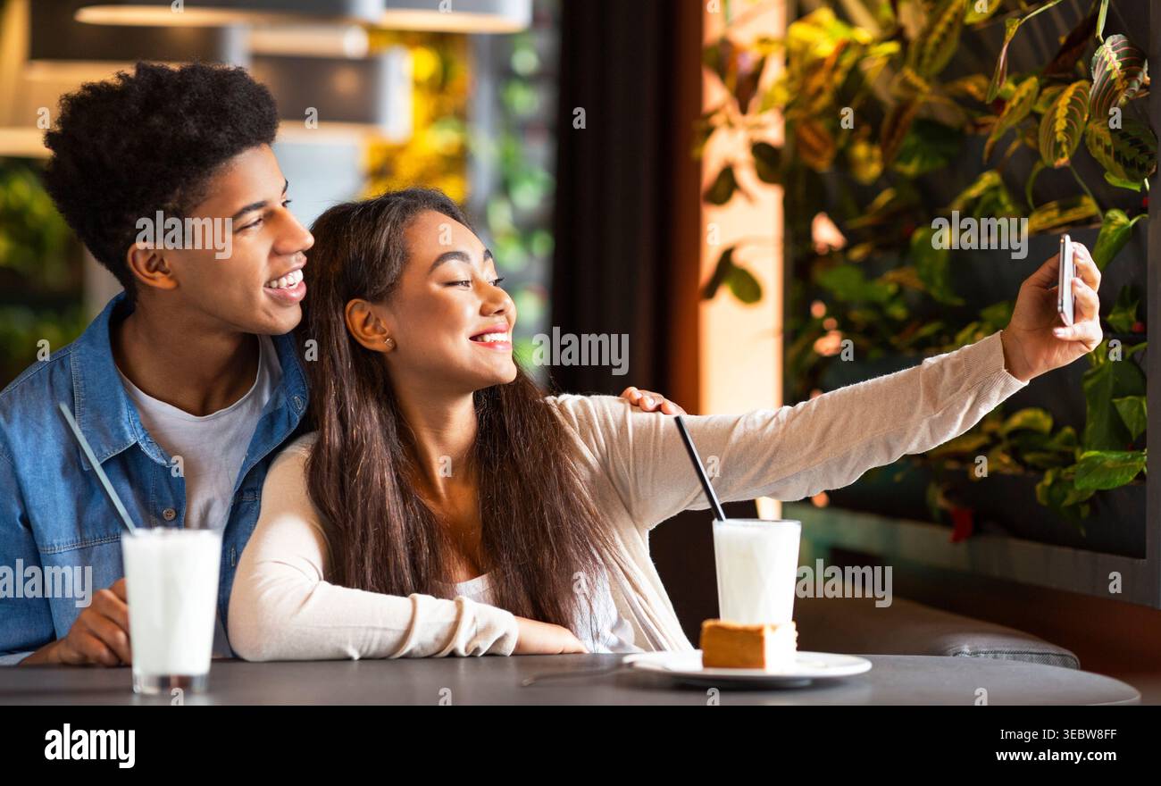 Junges Paar genießt süße Momente und nimmt Selfie im Cozy Cafe mit Getränken und Dessert Stockfoto