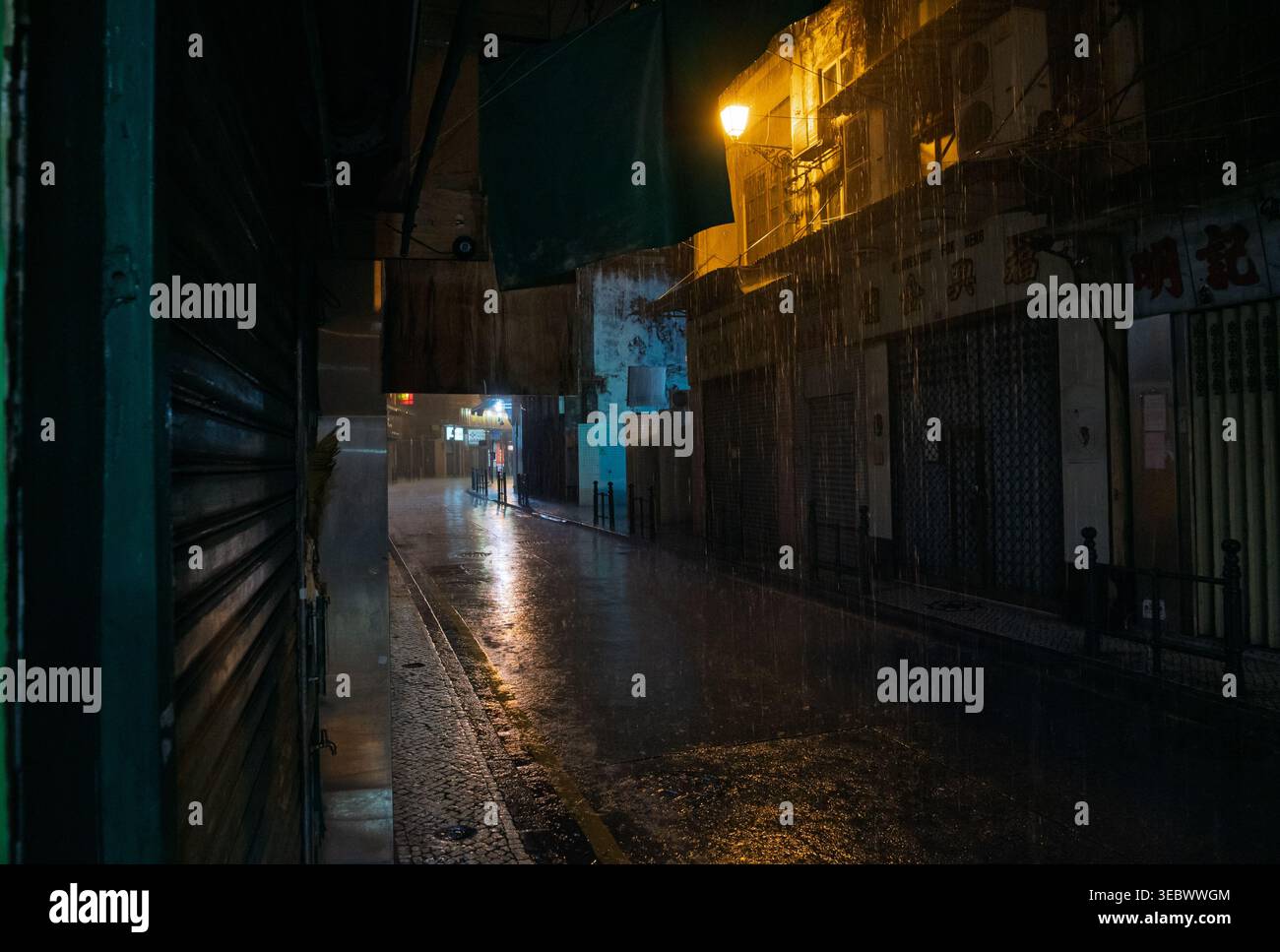 Macau, China - 8. Mai 2018: Ruhige Macau-Straße, beleuchtet von warmen Straßenlaternen unter ständigem nächtlichem Regen, nassem Straßenbelag Stockfoto