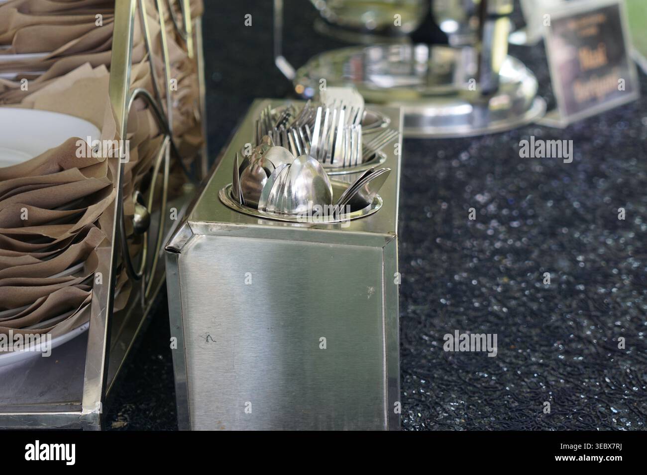 Ordentlich angeordnete Edelstahl-Utensilien und stapelbare Teller mit Servietten in Catering-Buffetform. Stockfoto