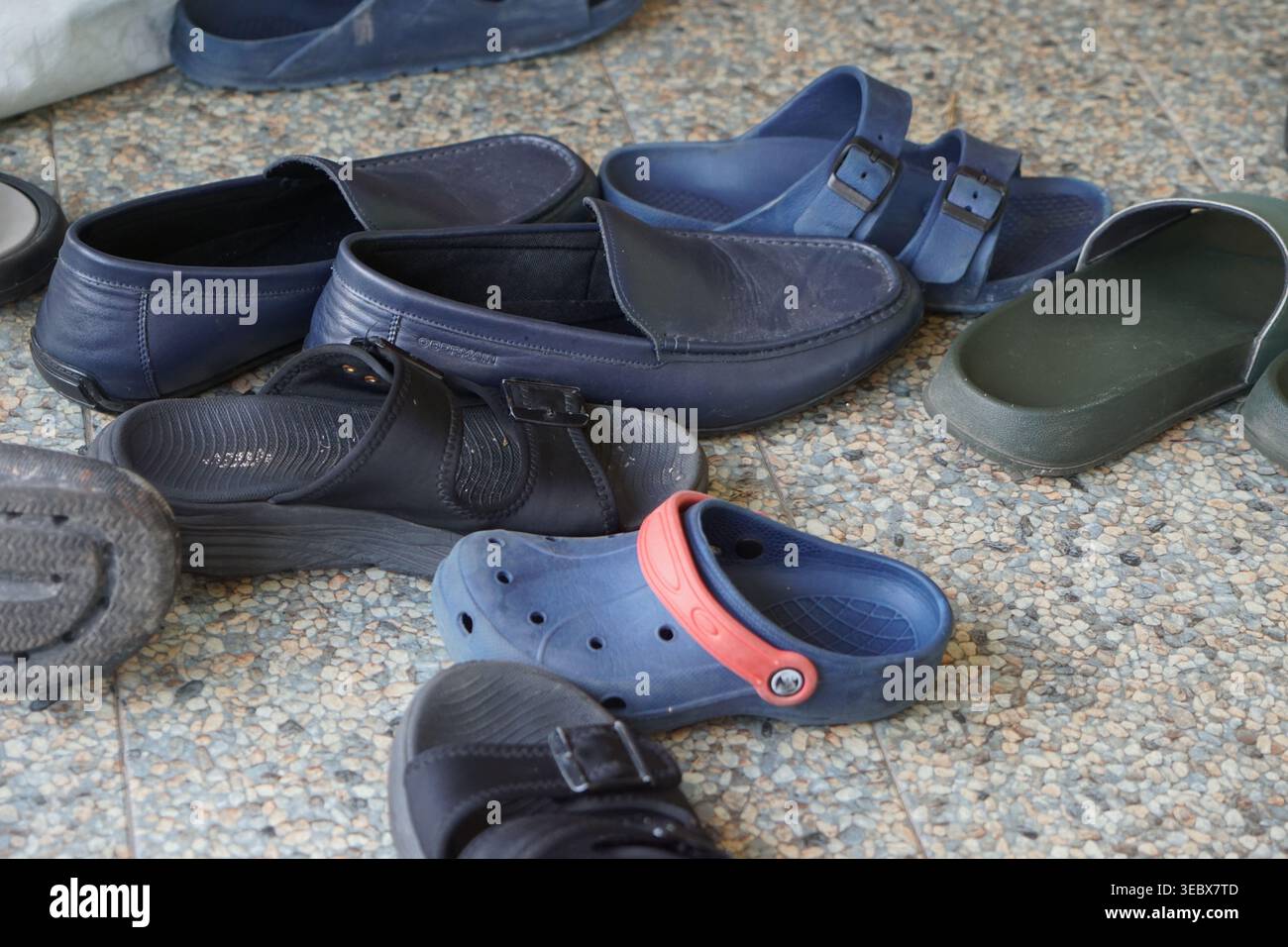 Mehrere Paar Schuhe und Sandalen verstreut auf Fliesenboden, alltägliche Szene auf malaiischen Hochzeiten oder Gemeindeversammlungen, bei denen die Gäste die Schuhe vorher ausziehen Stockfoto
