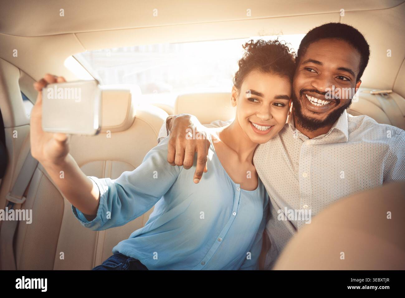Ein Paar nimmt ein Selfie zusammen auf dem Rücksitz eines Autos während eines sonnigen Tages Stockfoto