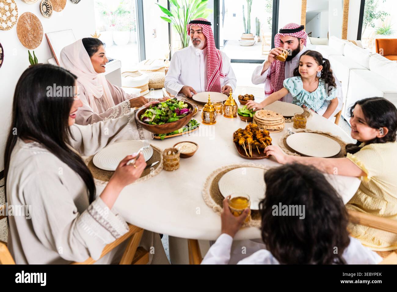 Arabische Familie versammelt sich an einem Esstisch, teilt eine Mahlzeit und genießt die Zweisamkeit, repräsentiert Traditionen und Lebensstil in einem modernen mittelösterreich Stockfoto