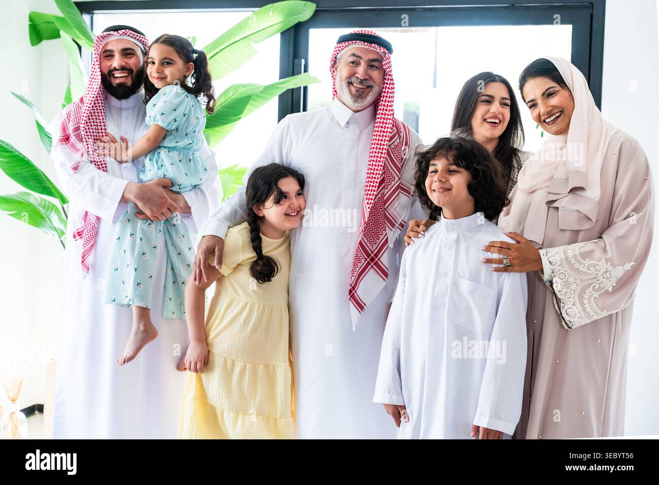 Die arabische Familie steht zu Hause zusammen, lächelt über Generationen hinweg und umschließt sie, zeigt warme Familienbande, kulturelle Kleidung und Stockfoto