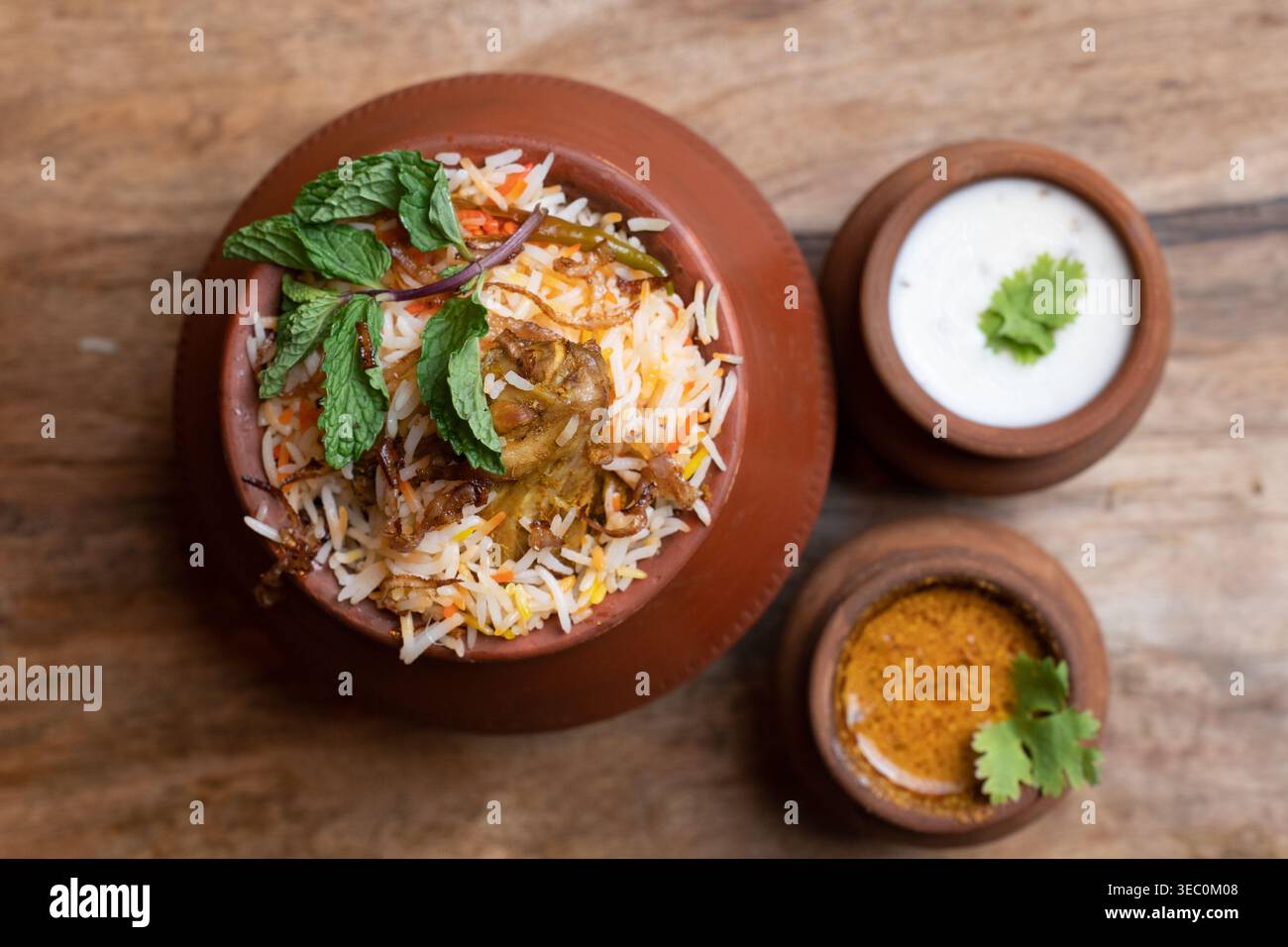 Ein einladender Blick von oben auf duftendes Hühnchen Biryani, das heiß in einem Erdtopf serviert wird. Es ist wunderschön garniert mit Pfefferminze und präsentiert mit zwei trad Stockfoto