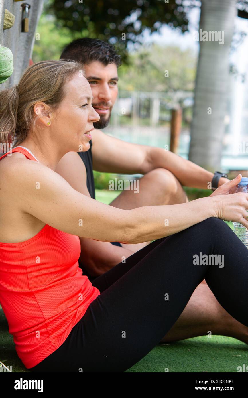 Ein Paar sitzt und ruht sich nach dem Training im Freien aus. Mann und Frau, die eine Pause machen, Wasser trinken und sich nach dem Training in einem Naturpark erholen Stockfoto