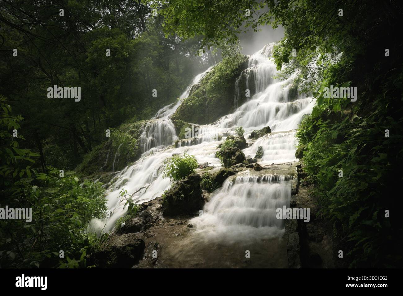 Wasserfall, der Klippen in einem düsteren, dunklen Wald herabstürzt. Eine traumhafte Landschaft mit Nebel und majestätischer Schönheit. Stockfoto