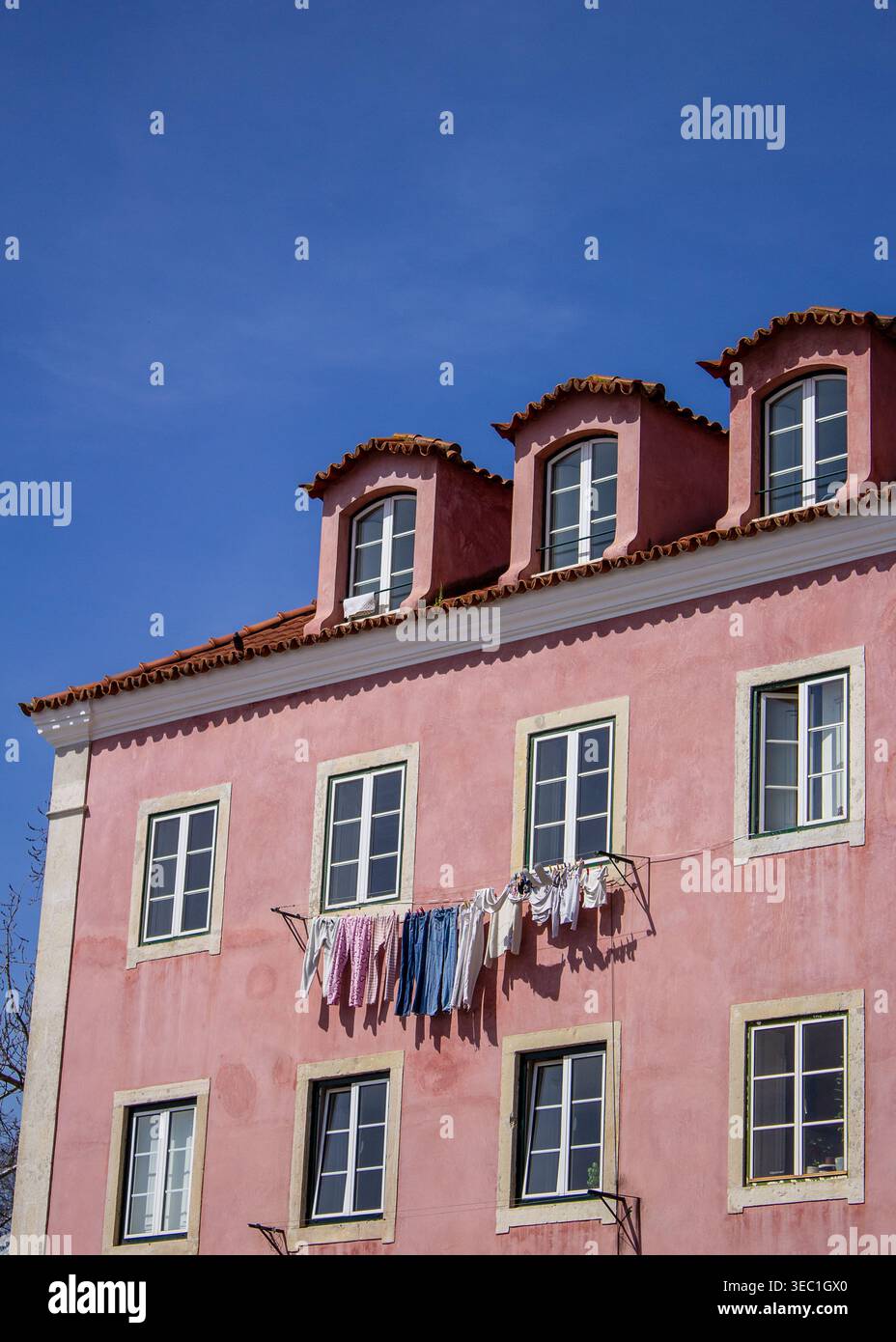 Die oberen Stockwerke eines pinkfarbenen Stuckgebäudes in Lissabon, Portugal, fotografiert vor einem tiefblauen Himmel. Eine Wäscheleine mit farbenfroher Wäsche. Stockfoto