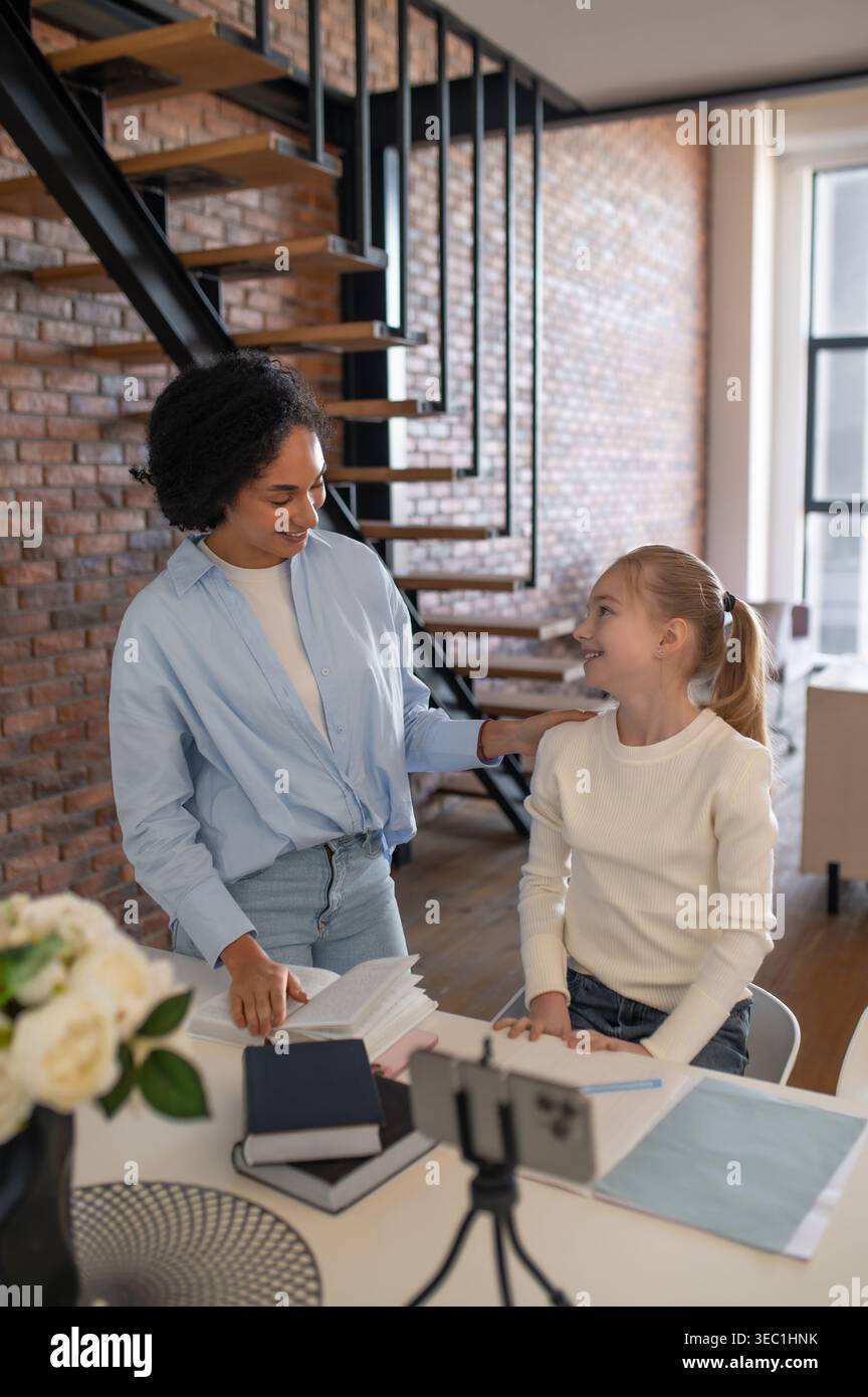 Weiße Frau mit Afro-Haaren, die Unterricht mit blondem Mädchen ausstrahlt Stockfoto