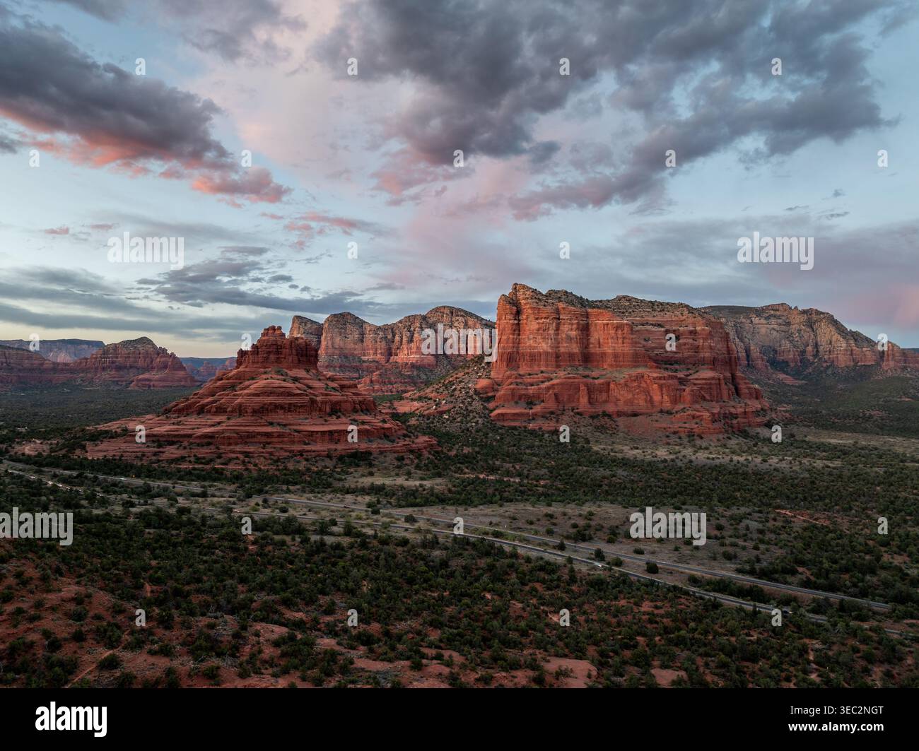 Blick aus der Vogelperspektive auf Bell Rock und Courthouse Butte in Sedona Arizona in der Abenddämmerung mit dramatischen Wolken und Highway durch das Wüstental Stockfoto