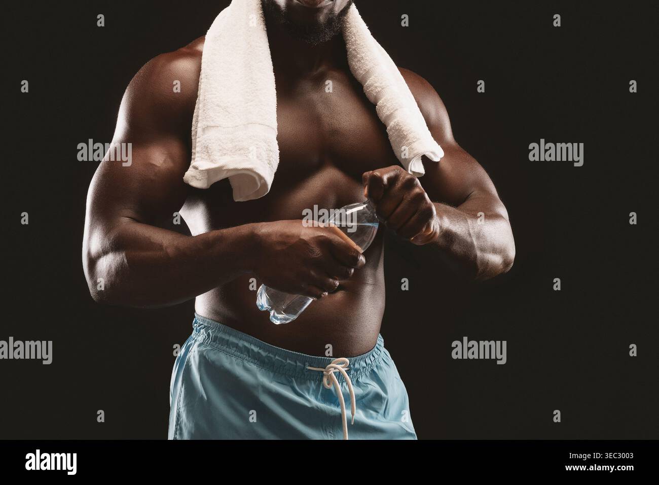 Der muskulöse Athlet kühlt sich nach dem Training ab und hält die Wasserflasche in der Fitnesseinstellung Stockfoto