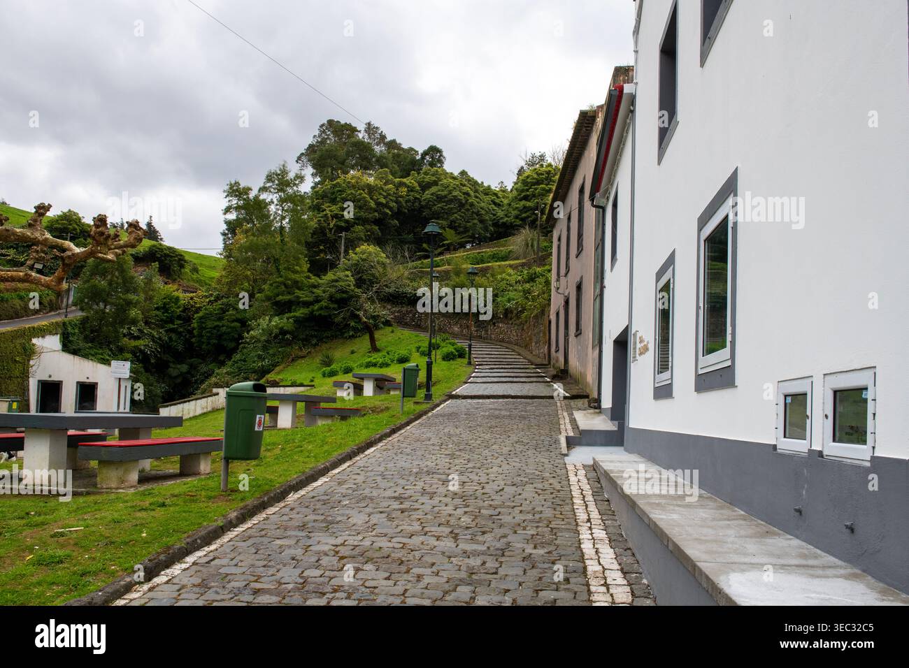 Friedliches Dorf auf den Azoren. Die kopfsteingepflasterte Straße schlängelt sich bergauf durch ein üppiges, grünes Dorf. Kleiner Park auf der linken Seite. Stockfoto