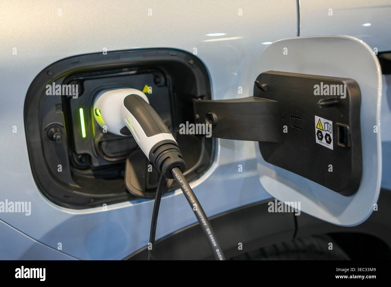 Nahaufnahme des weißen Ladeanschlusses für Elektrofahrzeuge mit eingestecktem Ladeanschluss und geöffneter Ladeklappe Stockfoto