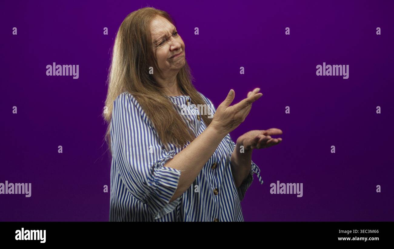 Frau Senior hispanic zeigt Zeigefinger mit gefaltetem Arm, sichtbarem Unterarm und Hand, trägt ein blau gestreiftes Hemd im lila Studio-Hintergrund; Missbilligung Stockfoto
