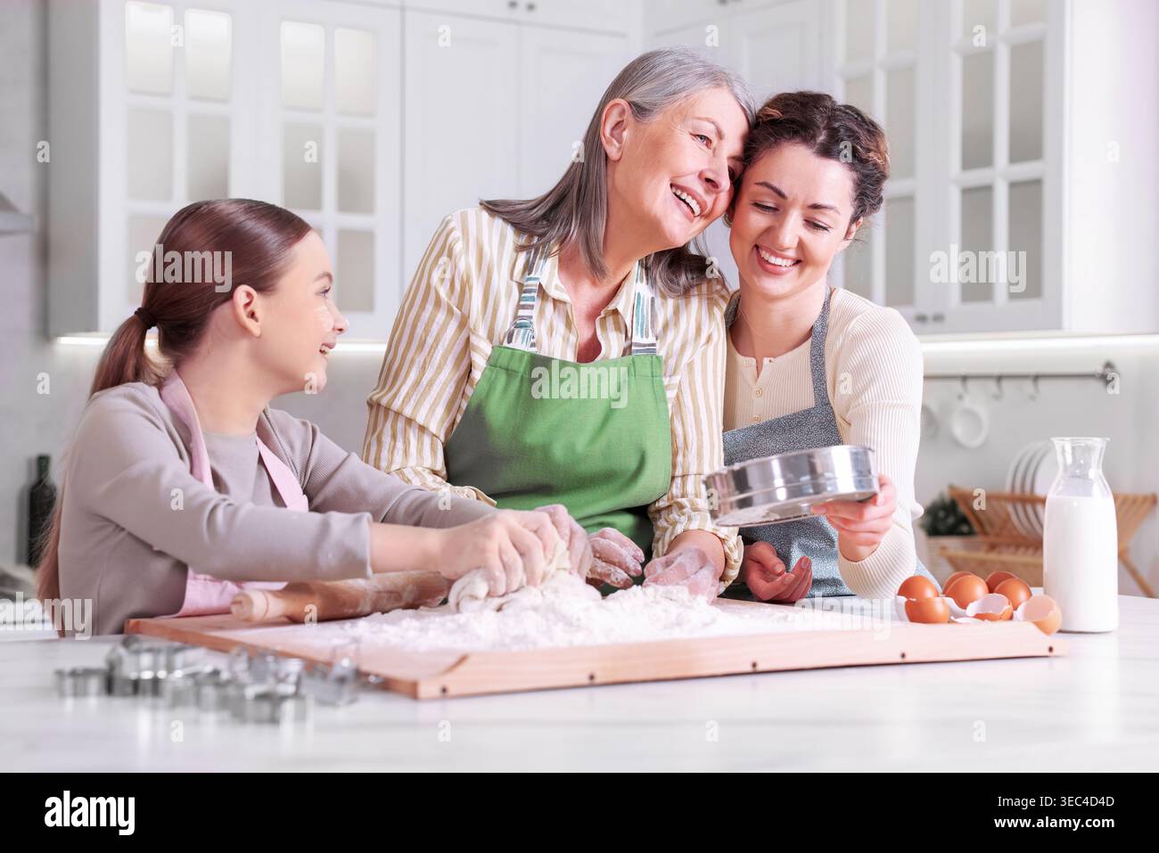 Glückliche Großmutter, ihre Tochter und Enkelin kochen zusammen am Tisch in der Küche Stockfoto