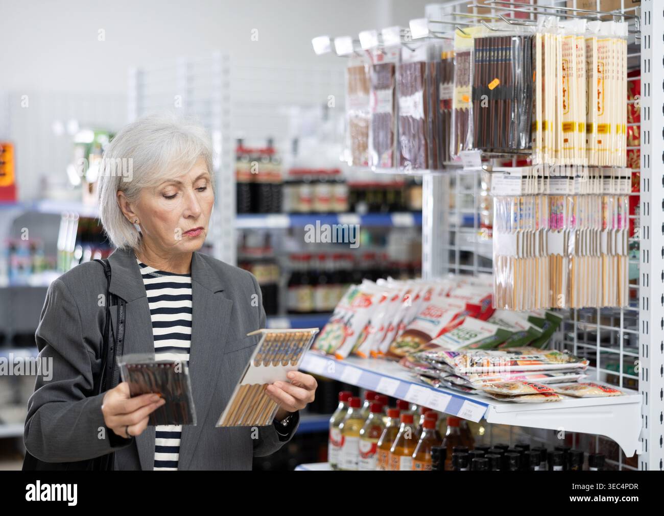 Reife Kundin wählt chinesische Essstäbchen in der orientalischen Warenabteilung. Stockfoto