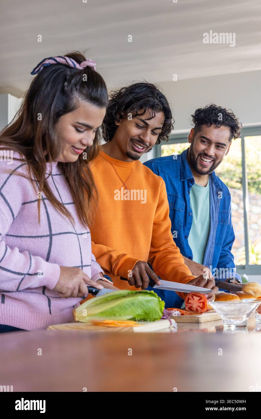 Verschiedene Freunde hacken Salat und schneiden Tomaten an der Küchentheke mit Messern und Brettern Stockfoto
