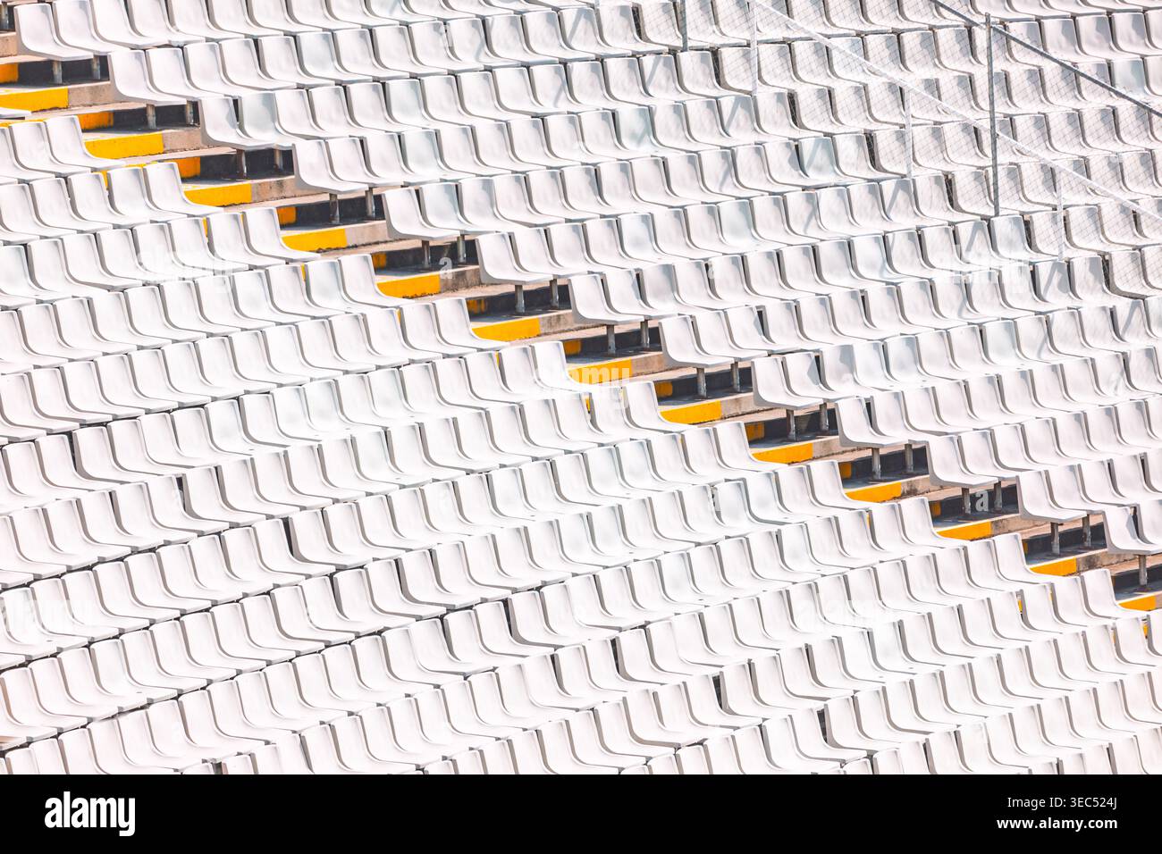 Reihen weißer Stadionsitze erzeugen ein geometrisches Muster, das von einer diagonalen Sitzreihe unterbrochen wird. Die sich wiederholende Sitzanordnung bildet eine markante Optik Stockfoto