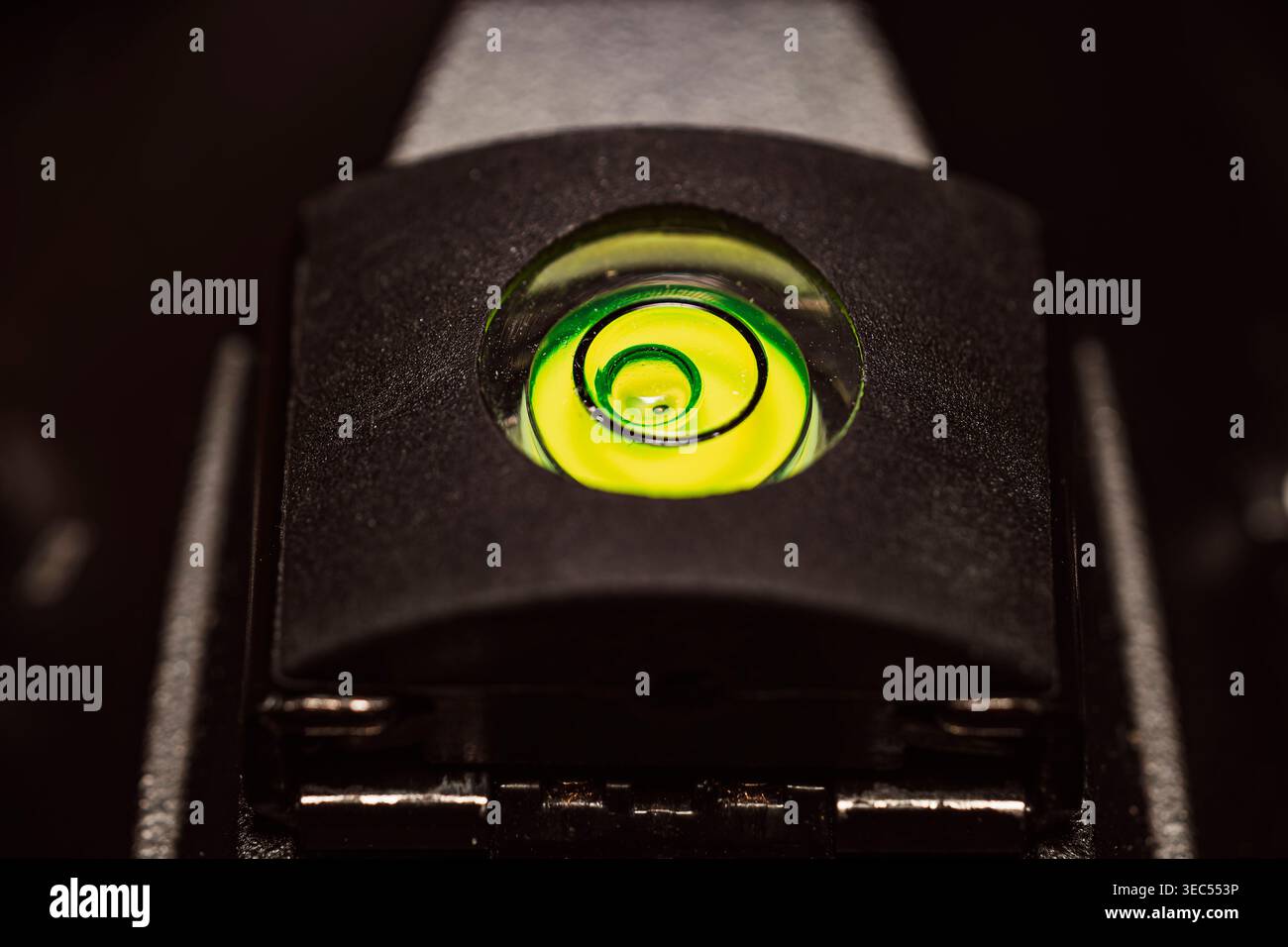 Extreme Makrofotos mit Fokus auf eine leuchtend grüne und gelbe kreisförmige Wasserwaage, die auf einem schwarzen Stativkopf bei schlechten Lichtverhältnissen montiert ist Stockfoto