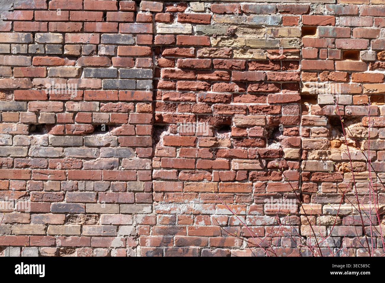 Verwitterte Ziegelwand mit verschiedenen Orangetönen, Zementlinien, Bohrlöcher und verfallene Ziegelsteine, die eine alte, gemauerte Öffnung in horizontaler Ansicht zeigen. Stockfoto