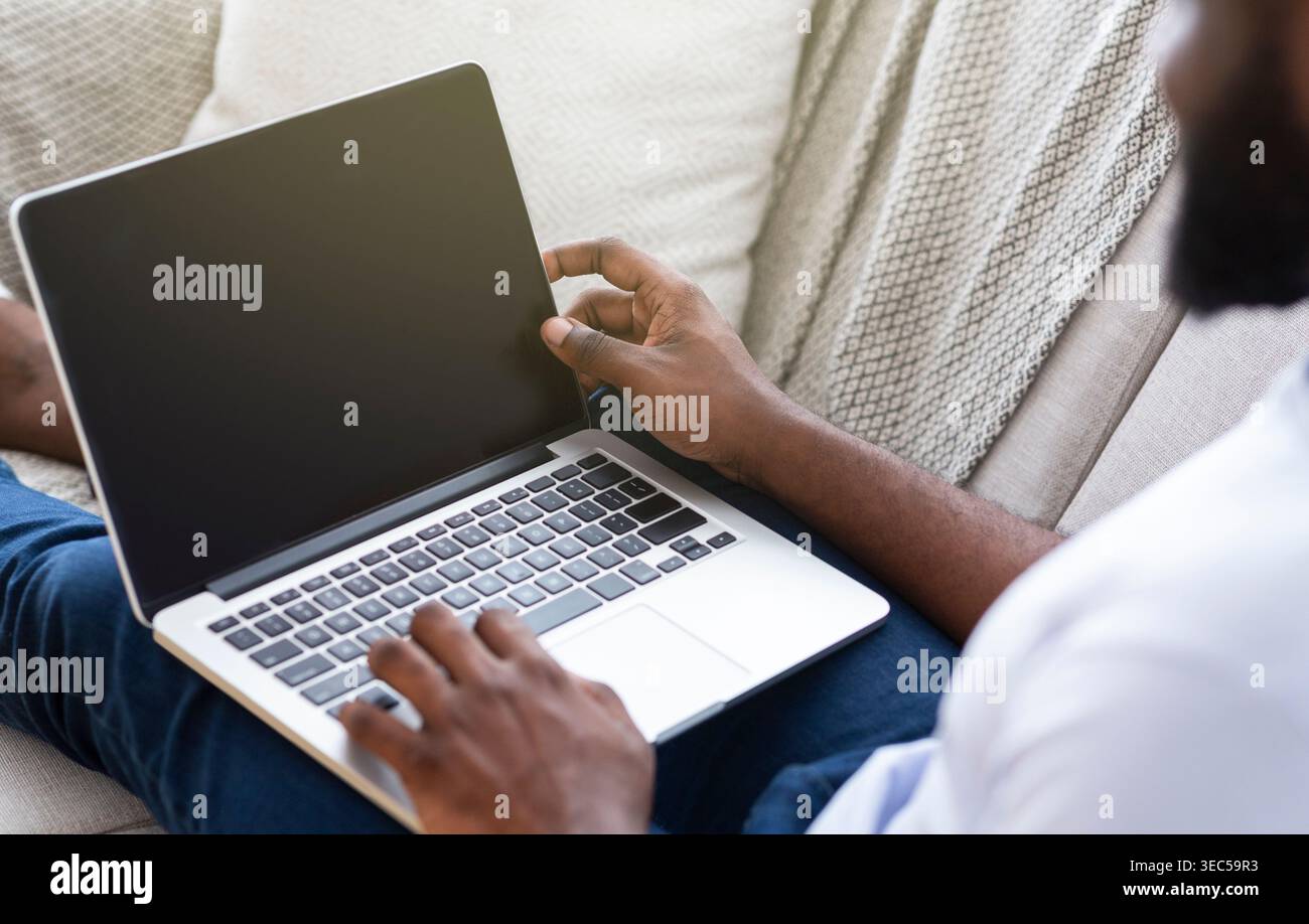 Einzelperson, die an einem Laptop arbeitet und dabei bequem auf einer Couch sitzt Stockfoto