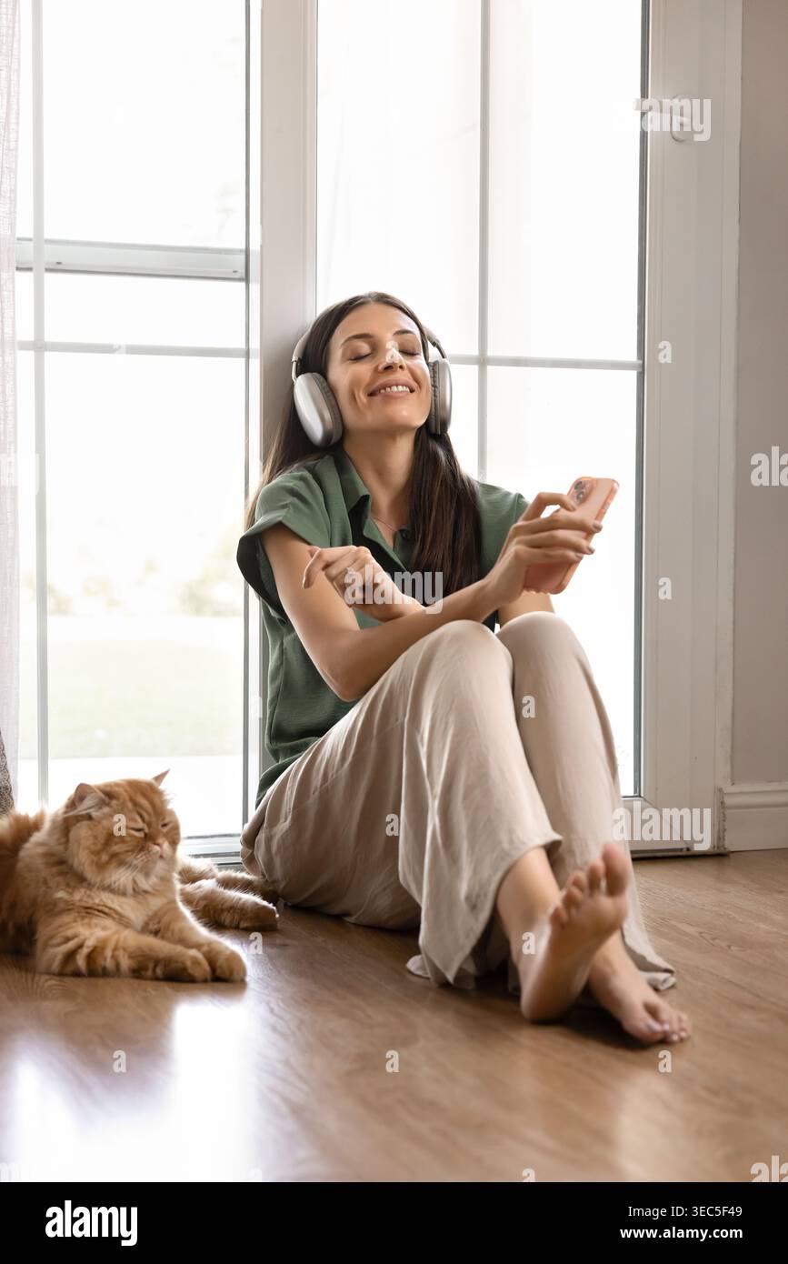 Frau, die Musik hört, sitzt auf dem Boden mit der Katze Stockfoto