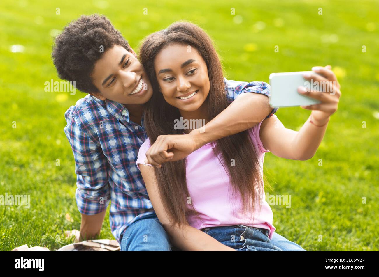Ein Paar macht ein Selfie, während er an einem sonnigen Tag auf dem Gras sitzt Stockfoto