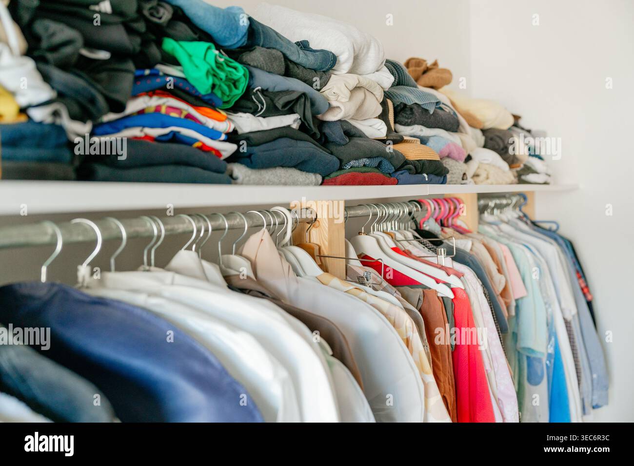 Der Schrank zeigt einen unordentlichen Haufen oben und die organisierte Kleidung unten. Vor- und Nachorganisation in der Hausgarderobe. Die Garderobe ist übersichtlich und ordentlich Stockfoto