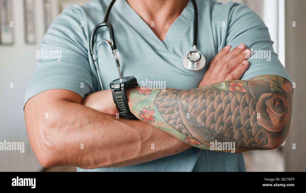 Tätowierter Arzt mit Stethoskop-Querarmen im Scrubs Porträt Stockfoto