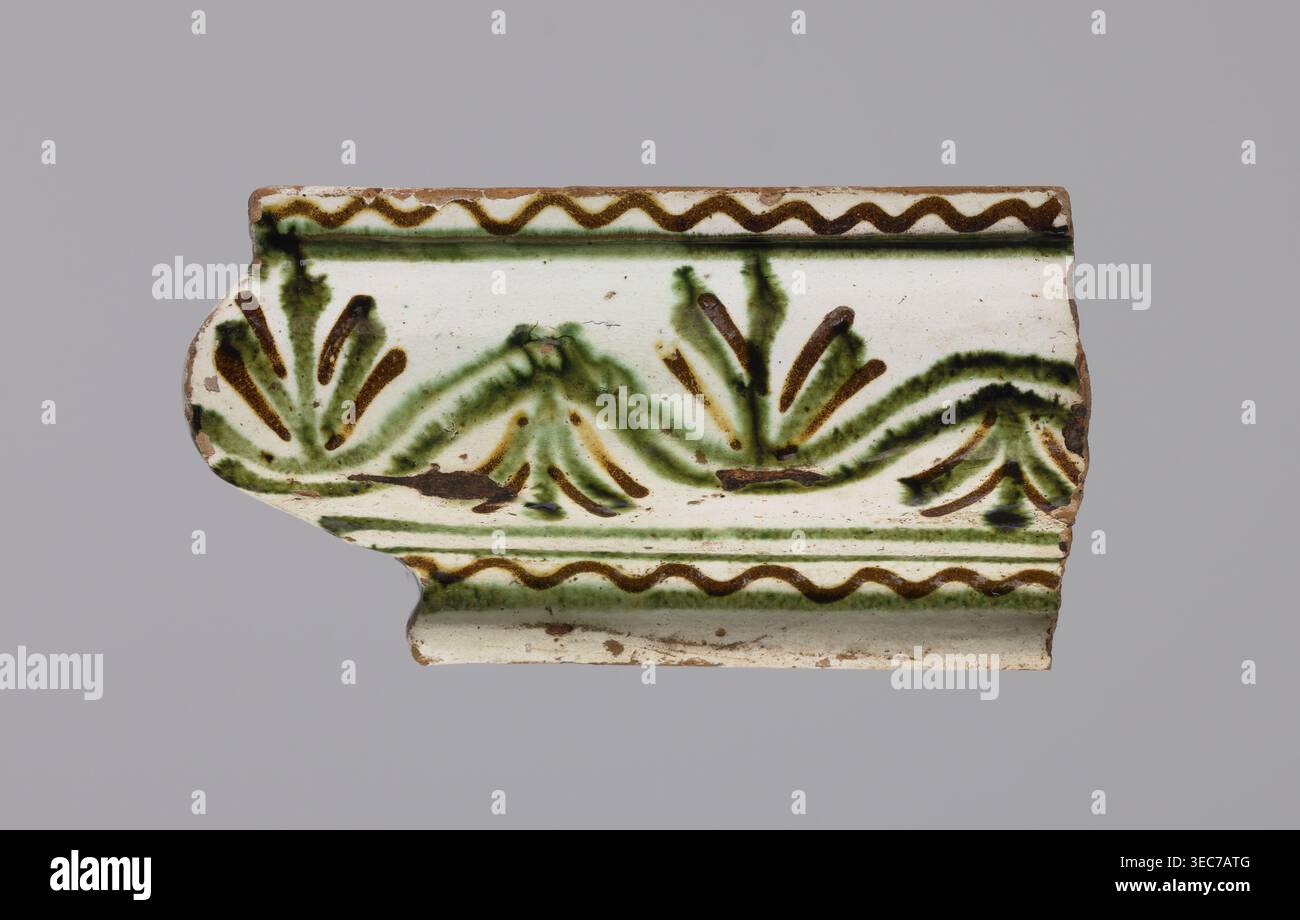 Gesimsfliesenfragmente 4, Fliesenscherben; gemalt mit gewelltem Wirbel; 19. Jahrhundert; Region Hutsul, Polen; Pflanzenschmuck; hergestellt für Herde, Ein Fragment einer dekorativen Keramikfliese mit weißem Hintergrund, das ein gemaltes Muster in Grün und Braun zeigt; das Fragment hat eine geschwungene Kante und einen gewellten oberen Rand in Braun, mit einer sich wiederholenden wellenförmigen braunen Linie und einer grünen Waschung darunter, und ein zentrales, blättriges oder fächerähnliches Motiv, das mit grünen Pinselstrichen und braunen Akzenten auf der Oberfläche dargestellt wird, mit abgenutzten Kanten und kleinen Flächen aus freiliegendem Ton in einer braunen Farbe, die alle gegen eine neutrale Farbe gesetzt sind Stockfoto