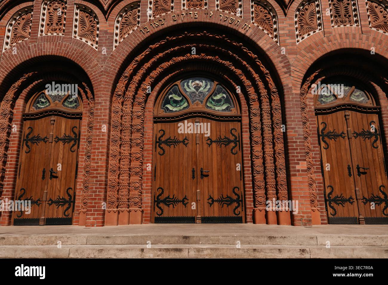 Verzierte hölzerne Eingangstüren der Subotica Synagoge in Subotica, Serbien. Dekorative Backsteinbögen und geschnitzte Details unterstreichen die historische Handwerkskunst. Stockfoto