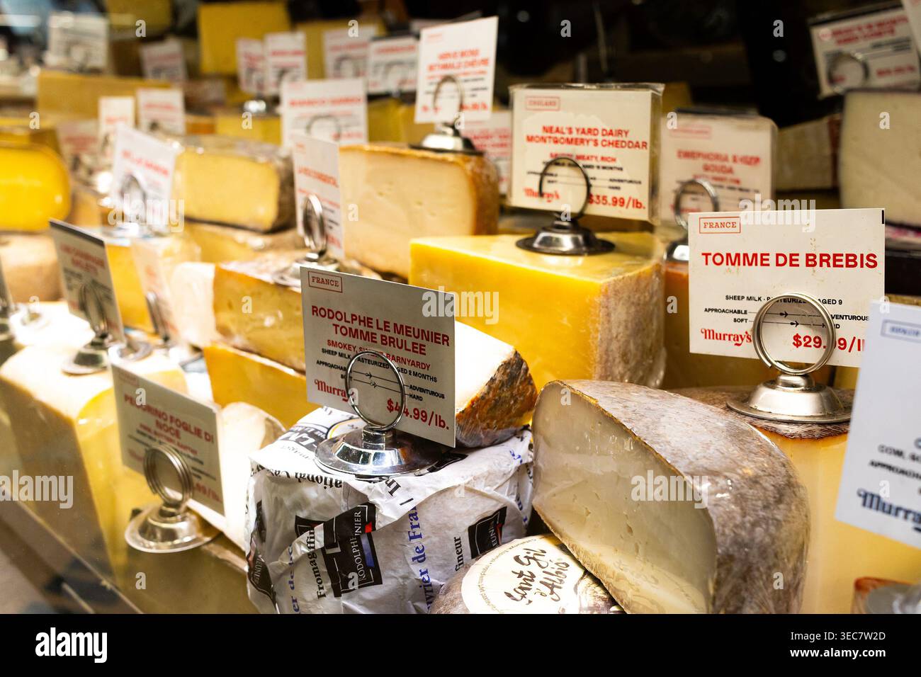 Käsespezialitäten in einem gekühlten Feinkostkasten mit Etiketten und Preisen bei Murray's Cheese in Manhattan, New York City Stockfoto