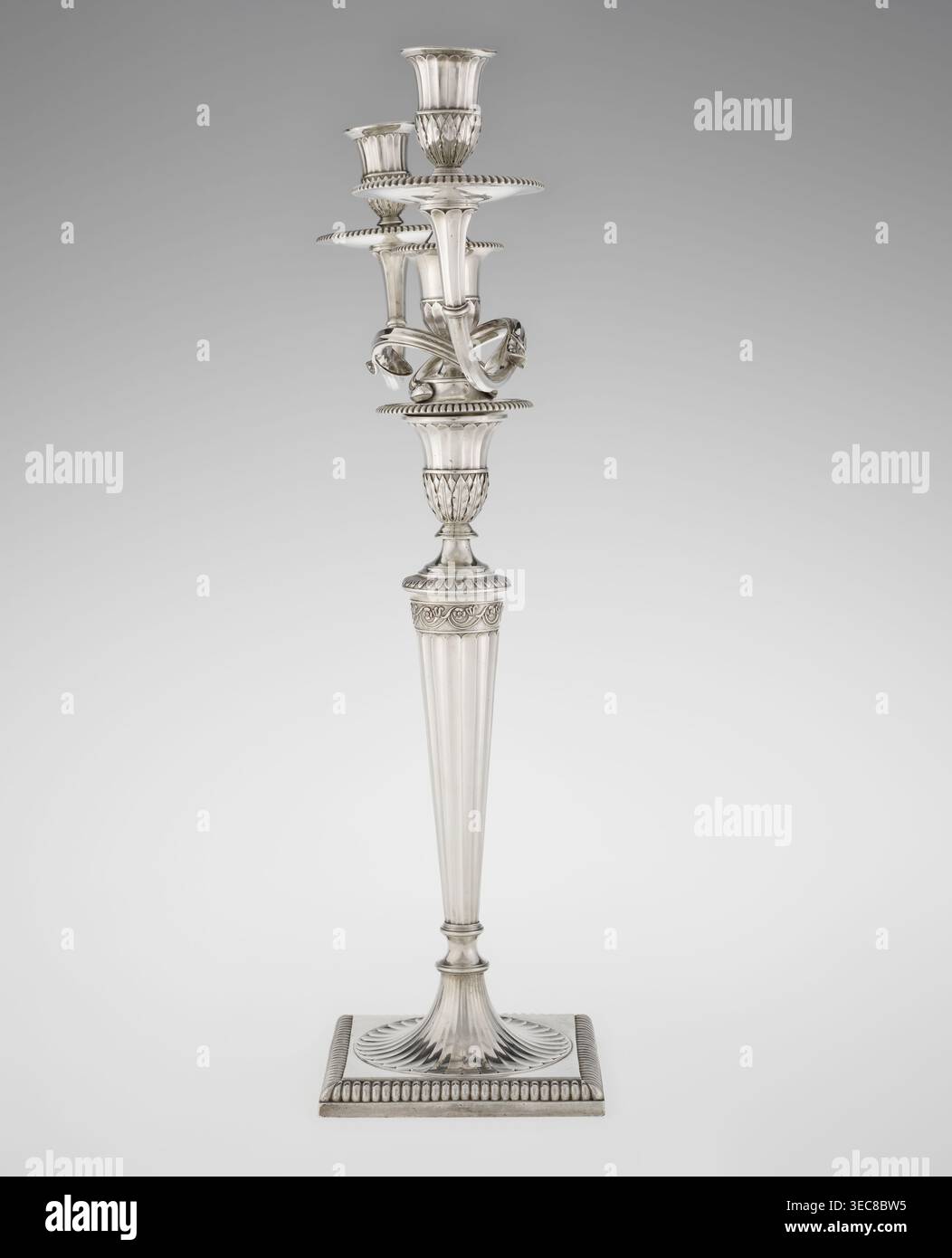 Klassizistische zweiarmige Kerzenleuchter, Schofield, John fl. 1776–1796 Goldschmied, klassizistischer Stil, Godron-Ornamente, Monogramme, Facettierung, klassizistischer zweiarmiger Kandelaber auf quadratischem Boden, umgeben von Godron-Ornamenten, geht in einen kreisförmigen Fuß über, der mit einer umliegenden Rosette verziert ist; facettierter Stiel, der oben mit einer gerändelten Blumenranke eingeschlossen ist, die in einem vasenförmigen Sockel endet, der mit Akanthusblättern und Facetten verziert ist, umrandet mit Godronen, in der Form zweier facettierter, drehbarer Arme, die mit plättchenförmigen Gewinnen und Vasen endet Stockfoto