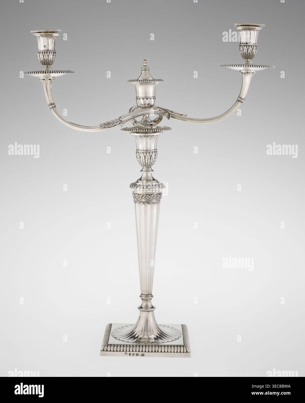 Klassizistische zweiarmige Kerzenleuchter, Schofield, John fl. 1776–1796 Goldschmied, Klassizismus, Godron Ornamente, Monogramme, Facettierung, klassizistischer zweiarmiger Kandelaber auf quadratischem Boden, umgeben von Godron-Ornamenten, geht in einen kreisförmigen Fuß über, der mit einer umliegenden Rosette verziert ist; facettierter Stiel, der oben mit einer gerändelten Blumenranke eingeschlossen ist, die in einem vasenförmigen Sockel endet, der mit Akanthusblättern und Facetten verziert ist, umrandet mit Godronen, in der Form zweier facettierter, drehbarer Arme, die mit plättchenförmigen Gewölben enden Kerzenvenen Vase und Kerzenvenen Vase Stockfoto