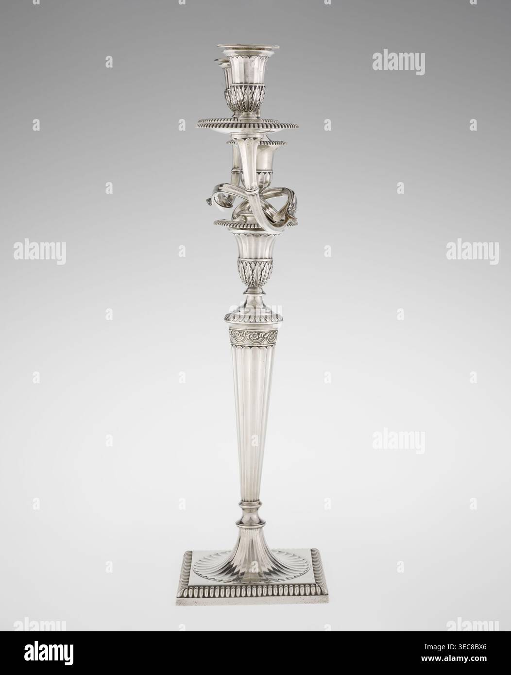 Klassizistische zweiarmige Kerzenleuchter, Schofield, John fl. 1776–1796 Goldschmied, klassizistischer Stil, Godron-Ornamente, Monogramme, Facettierung, hinterlässt Ornament, Georgier, Georg III., klassizistischer zweiarmiger Kandelaber. Auf einem quadratischen Sockel, umgeben von einem Godron-Ornament, der in einen kreisförmigen Fuß geht, der mit einer umliegenden Rosette verziert ist; facettierter Stiel, der oben mit einer gerändelten Blumenranke umschlossen ist und in einem vasenförmigen Sockel endet, der mit Akanthusblättern und Facetten verziert ist, umrandet mit Godrons, in dem eine Fassung in Form von zwei facettierten, drehbaren Armen gesetzt ist, die mit profilierten Schüsseln enden Tellförmigen Schalen und Vasen- Stockfoto