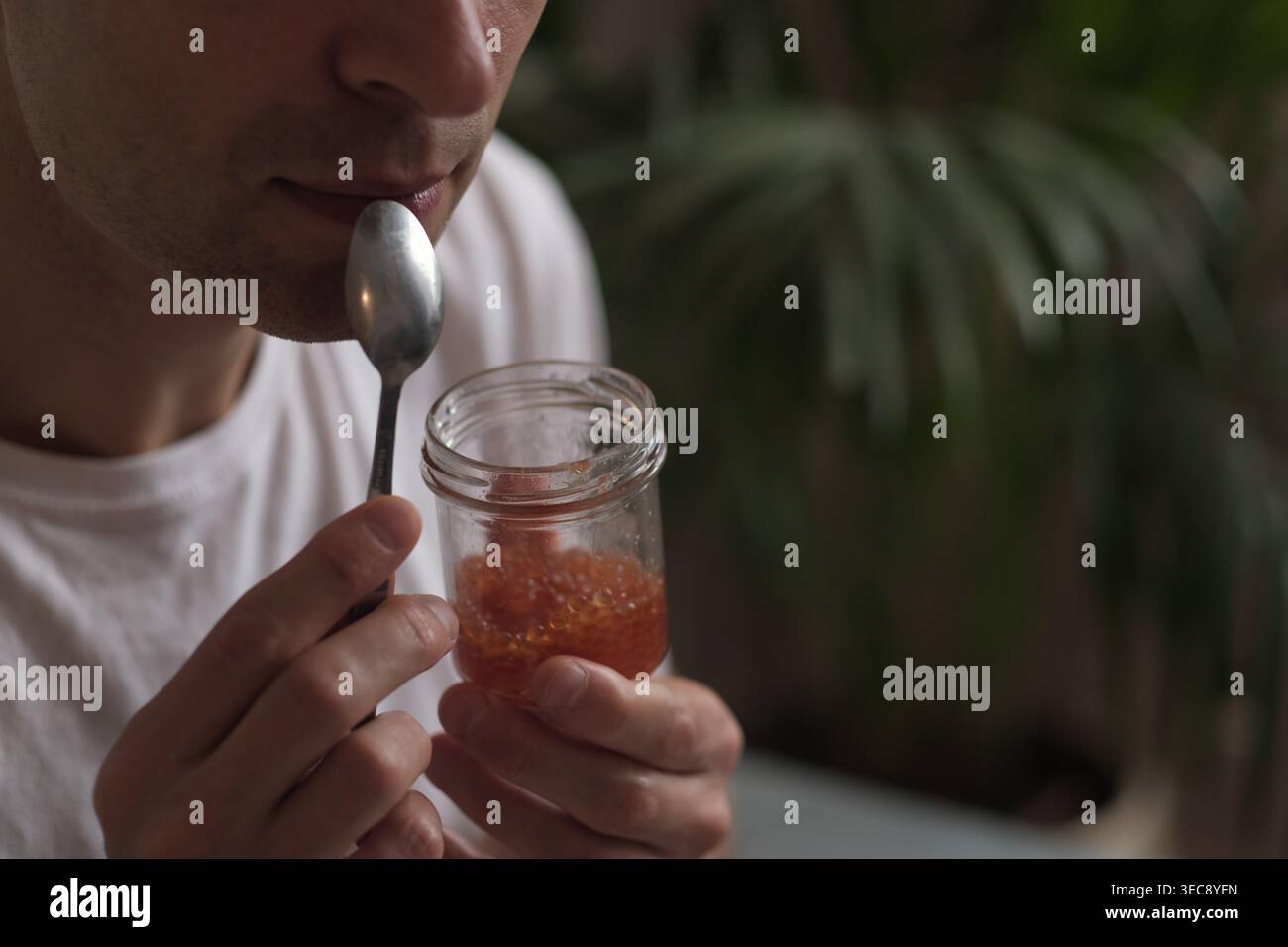 Ein Mann mit einem Glas Lachskaviar hält an ruhigem Tageslicht vor der Verkostung inne. Das Foto verbindet luxuriösen Minimalismus, Achtsamkeit und Authentizität Stockfoto