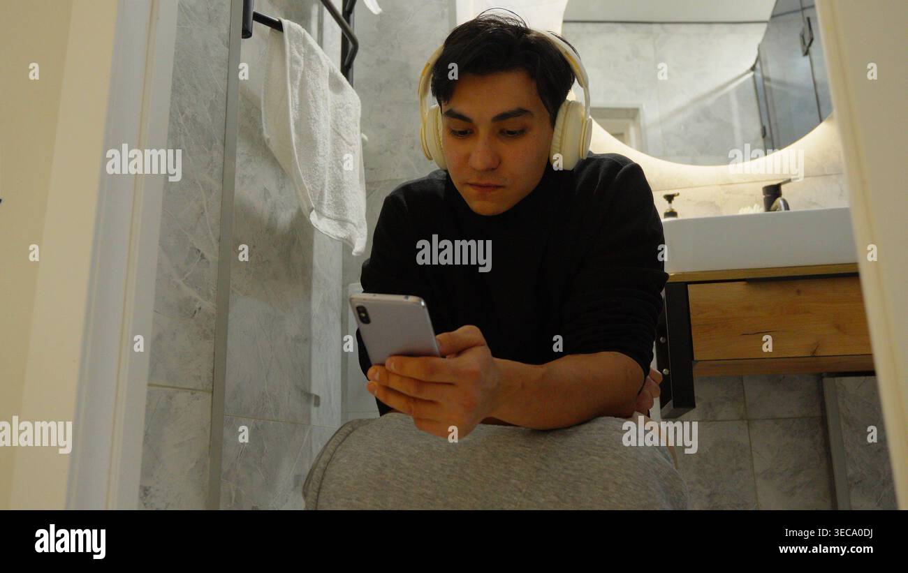 Mann, der sein Smartphone im dunklen Badezimmer benutzt Stockfoto