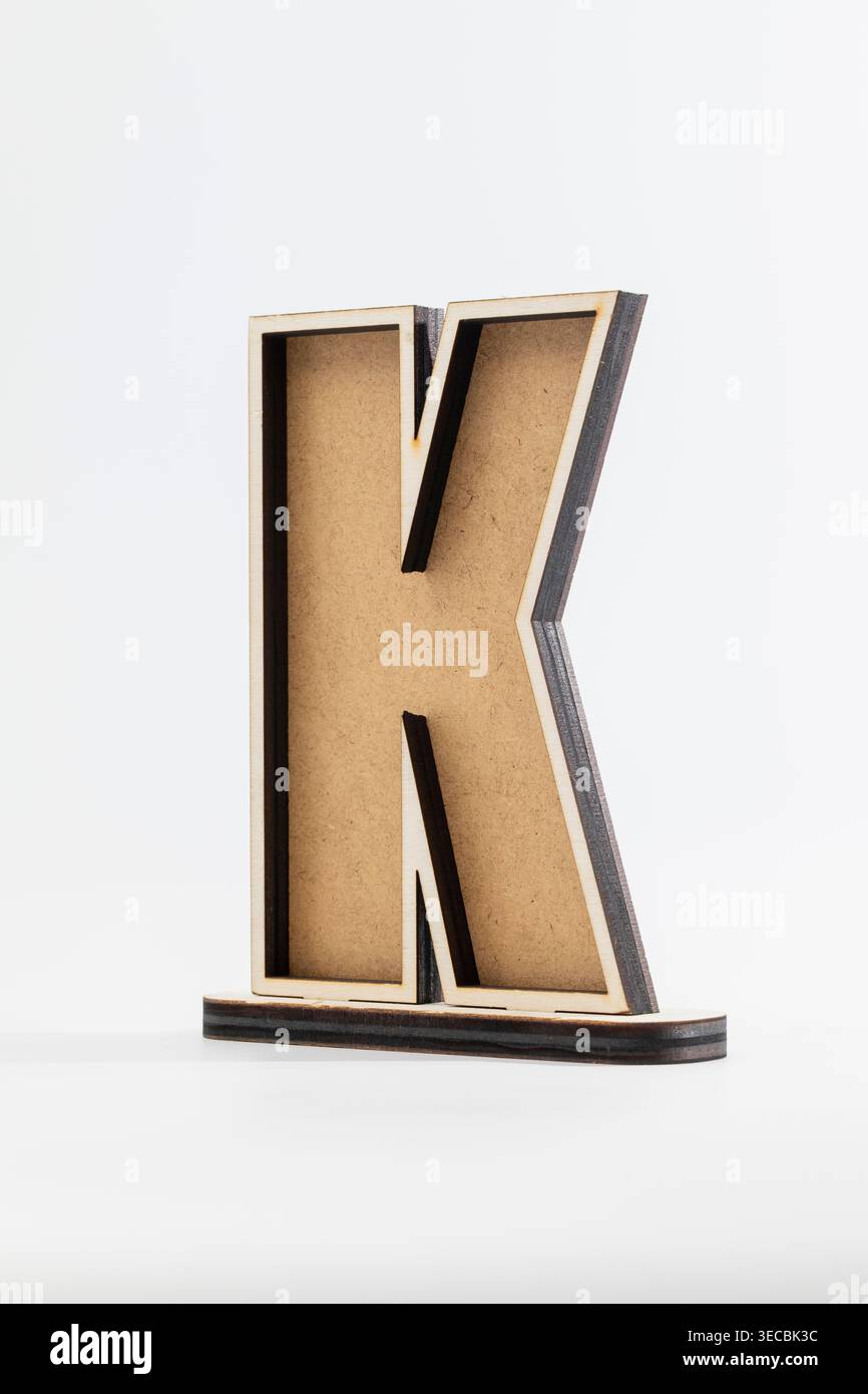 Der minimalistische Holzbuchstabe „K“ steht aufrecht. Hellbraune Körnung steht im Kontrast zu dunklen Kanten. Sauberer weißer Hintergrund verbessert die moderne Ästhetik. Perfekt für Stockfoto