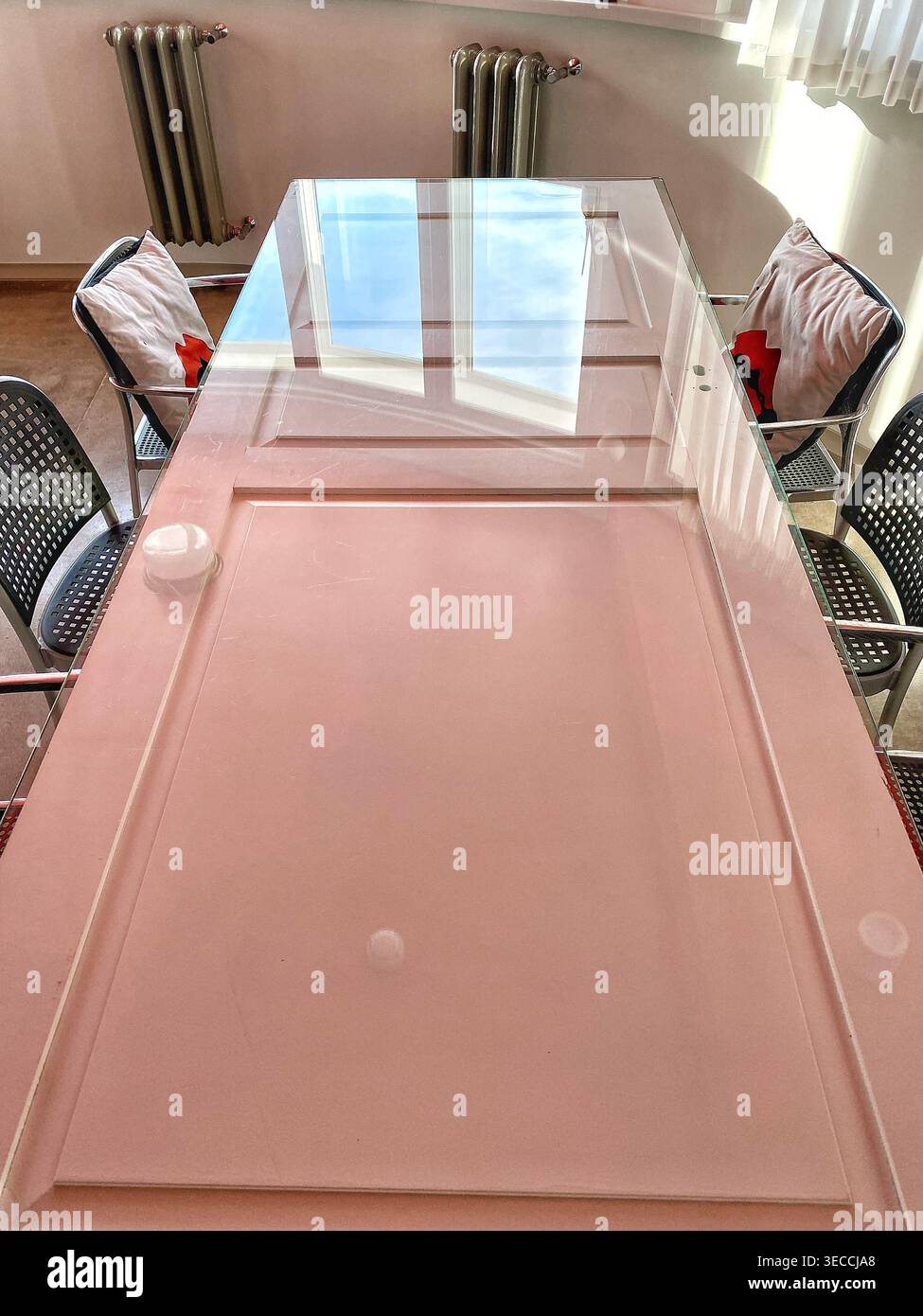 Moderner Besprechungstisch mit Glasoberfläche und Stuhl-Reflektionen, minimaler Büroinnenraum mit sanften Farben und natürlichem Licht - Smartphone-aufgenommenes Stockfoto