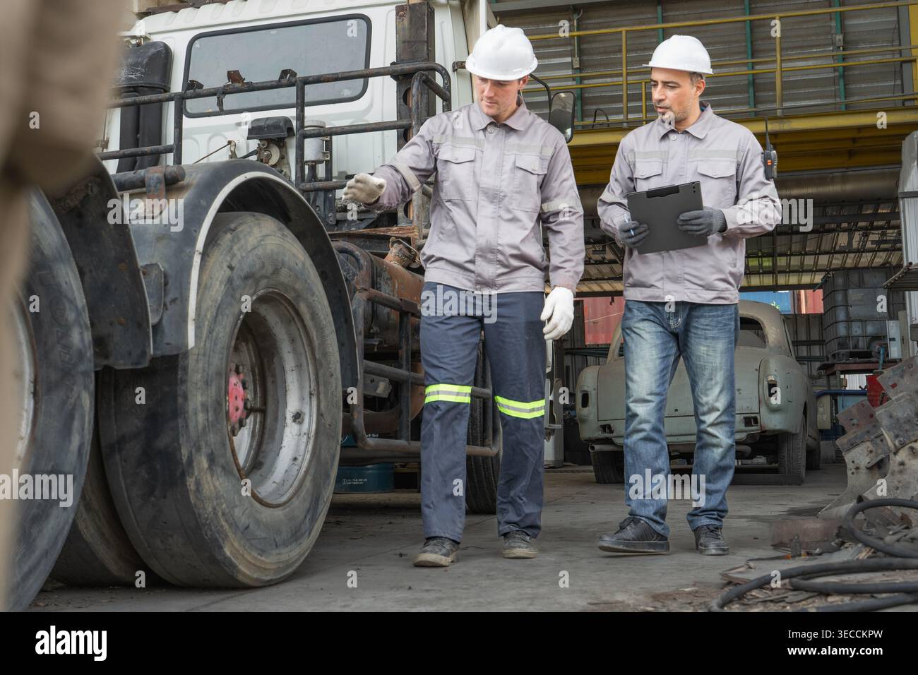 Kaukasische und mittelgroße männliche Techniker aus dem Nahen Osten gehen durch einen asiatischen Containerhof, während sie ein Klemmbrett halten, das für Routineinspektionen steht Stockfoto