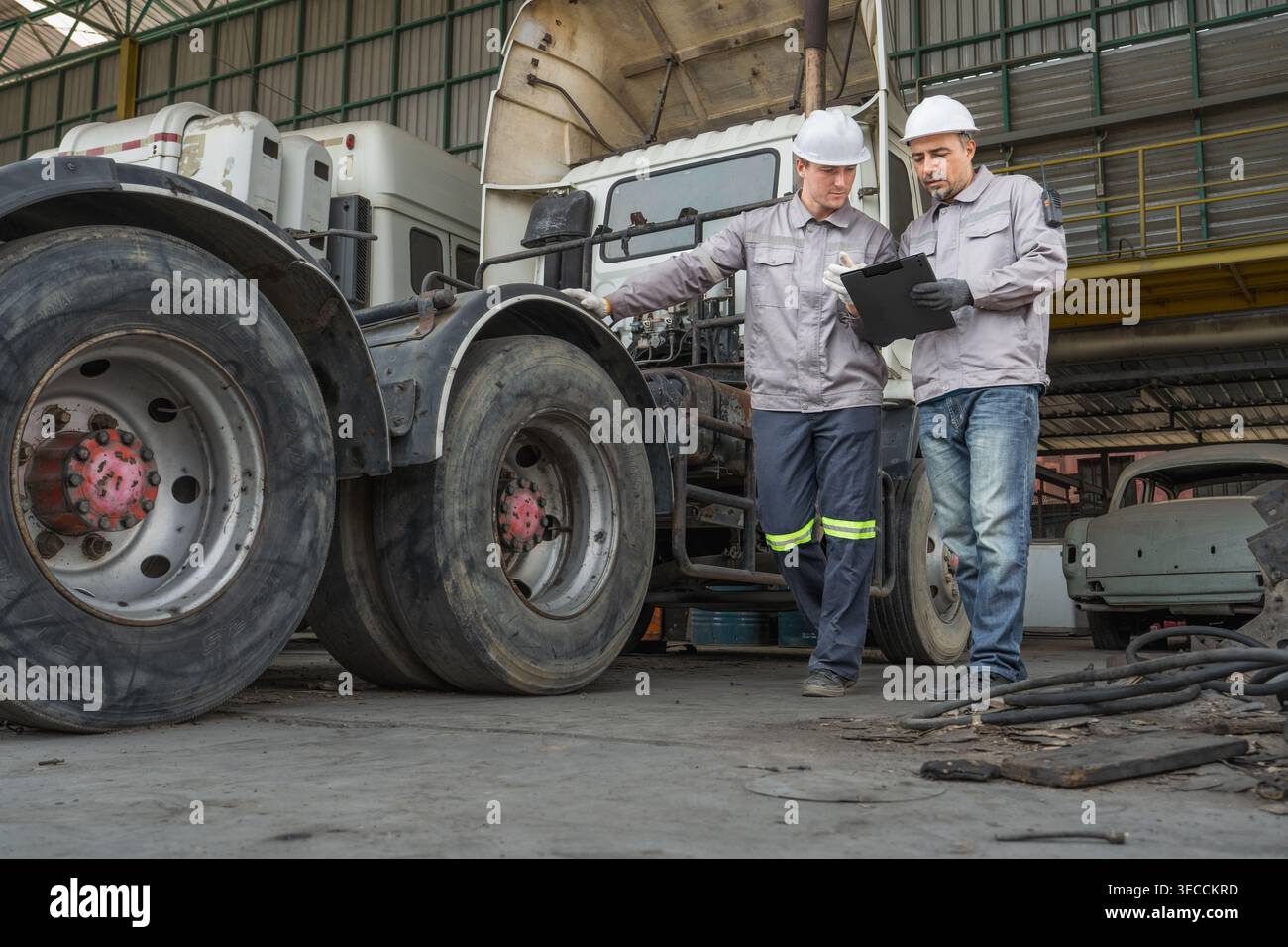 Kaukasische und mittelgroße männliche Techniker aus dem Nahen Osten gehen durch einen asiatischen Containerhof, während sie ein Klemmbrett halten, das für Routineinspektionen steht Stockfoto