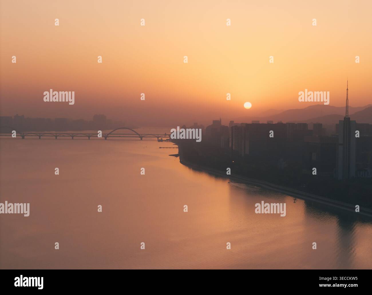 Wunderschöner Sonnenuntergang über dem Fluss mit orangefarbenem Leuchten, das auf Wasser und Brücken reflektiert Stockfoto