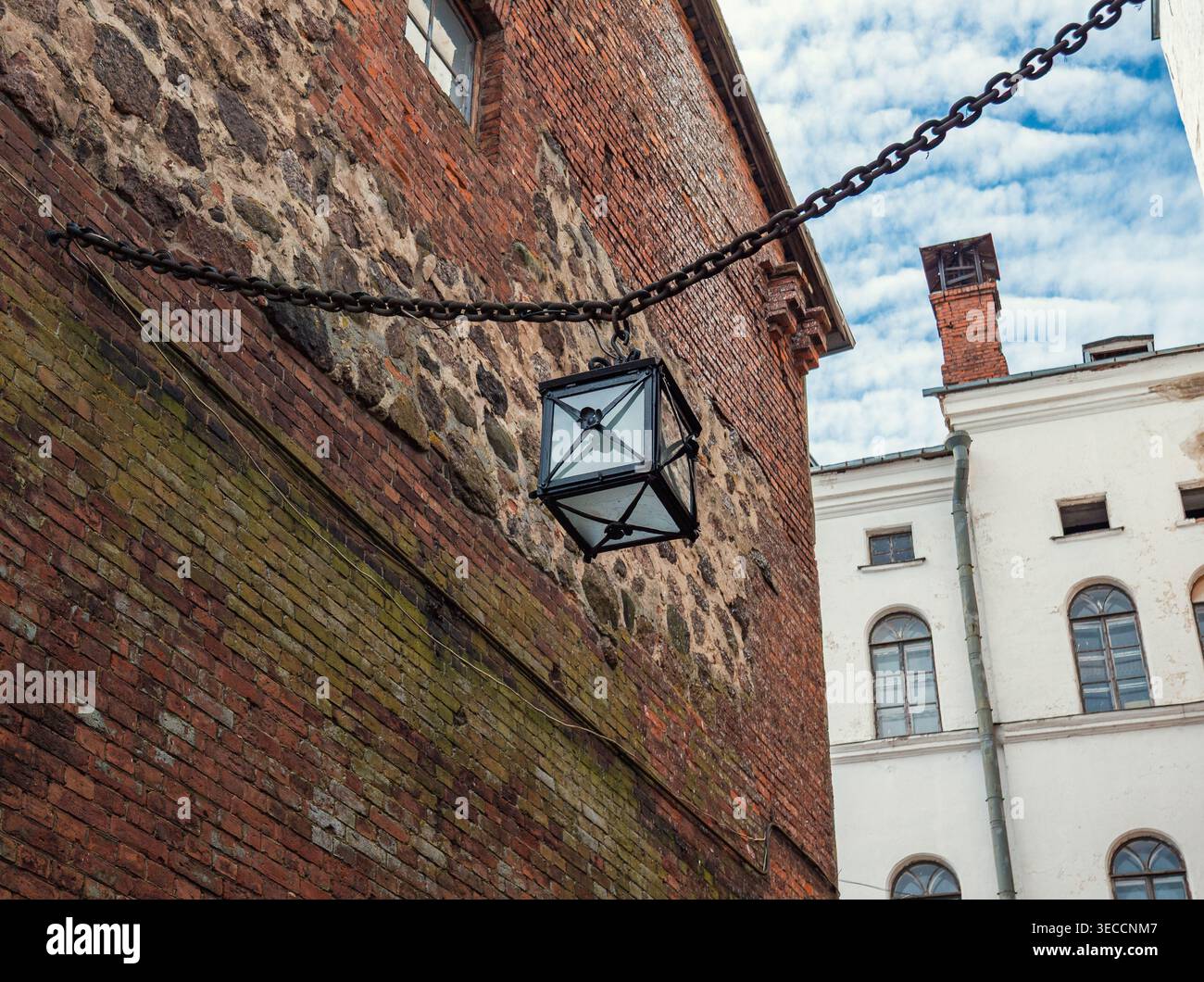 Eine Vintage-Laterne aus Metall hängt an einer schweren Kette an einer verwitterten Mauerwand aus Ziegeln und Stein und zeigt europäische Architektur Stockfoto