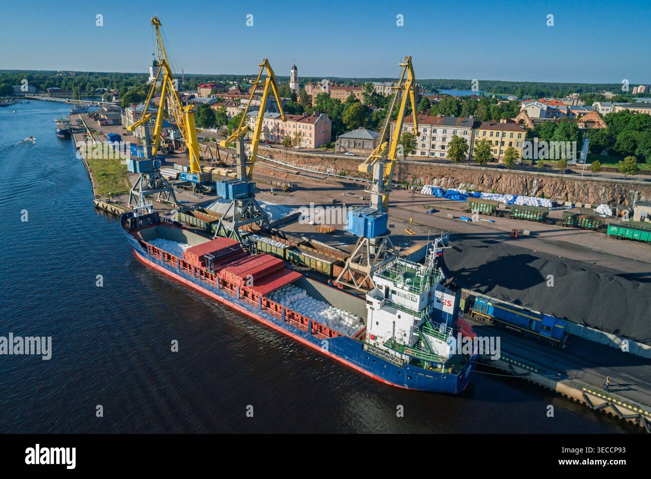 Massengutschiffen an einem Industriehafen angedockt, große gelbe Kräne und Zugwagen transportieren die Fracht bei Tageslicht Stockfoto