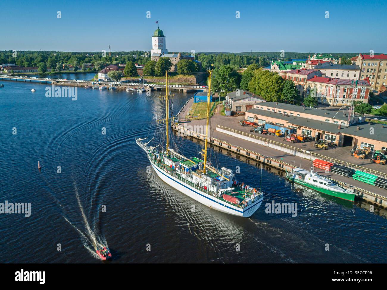 Vyborg, Russland - 4. Juli 2021: Großes weißes Segelschiff verlässt den Hafen von Vyborg mit dem historischen St. Olaf's Tower in der Ferne auf einer hellen Sonne Stockfoto