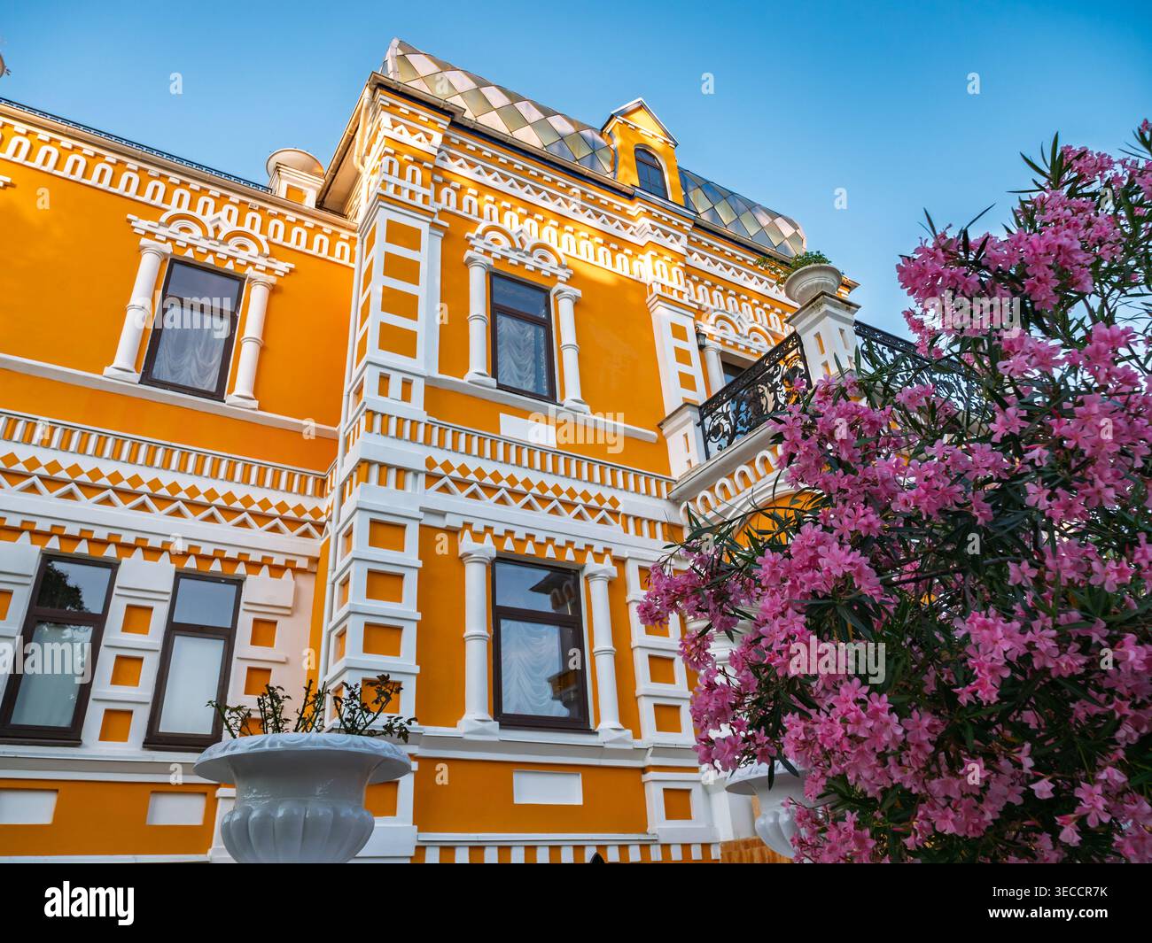 Großes oranges Herrenhaus mit raffinierter Architektur mit weißen dekorativen Details und einem blühenden Baum Stockfoto
