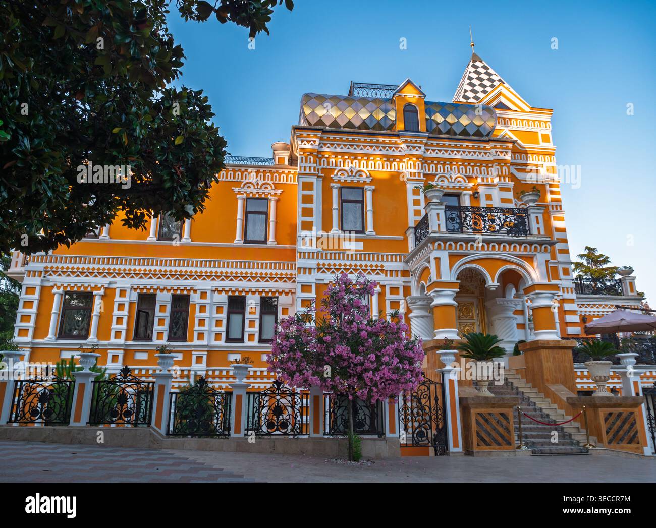 Großes oranges Herrenhaus mit raffinierter Architektur mit weißen dekorativen Details und einem blühenden Baum Stockfoto