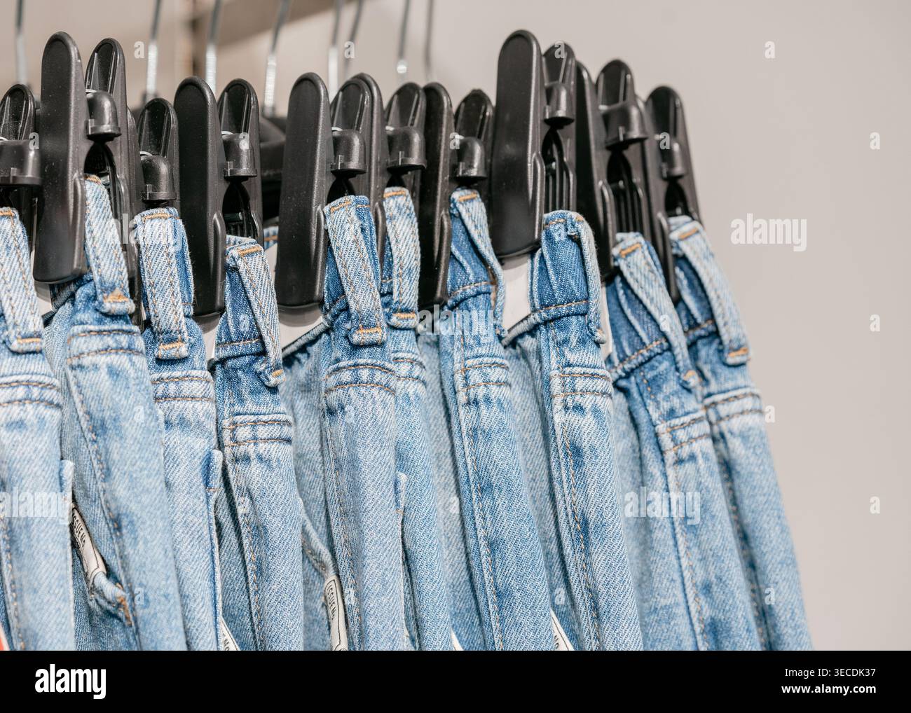 Denim-Overalls hängen am Regal im Laden. Ausstellungskonzept für Mode- und Einzelhandelsbekleidung für Kinder. Reihe blauer Denim-Overalls auf Kleiderbügeln. Lässiger Stil und Stockfoto
